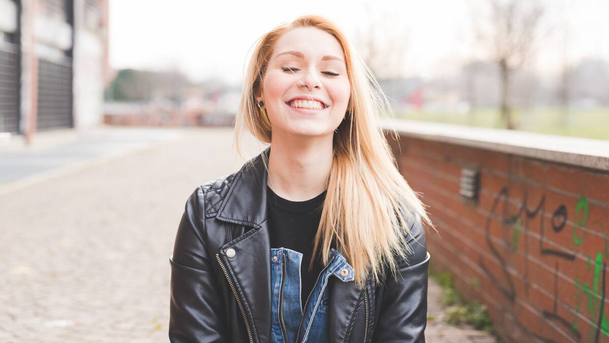 A woman standing outside, eyes closed, smiling.