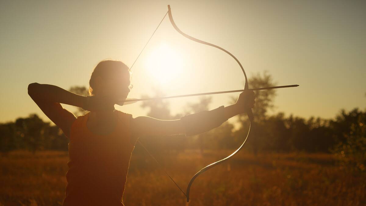 A heavily silhouetted image of a woman drawing back a traditional-style bow, the sun behind her.