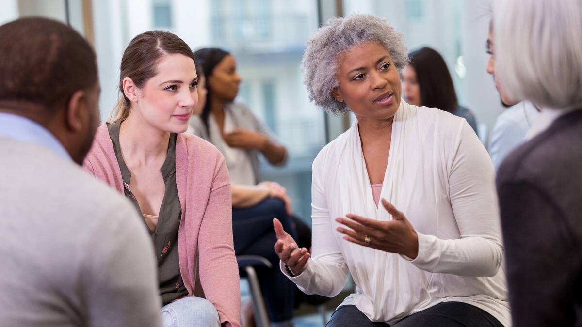 A woman speaking to a group of coworkers, gesturing with her hands.