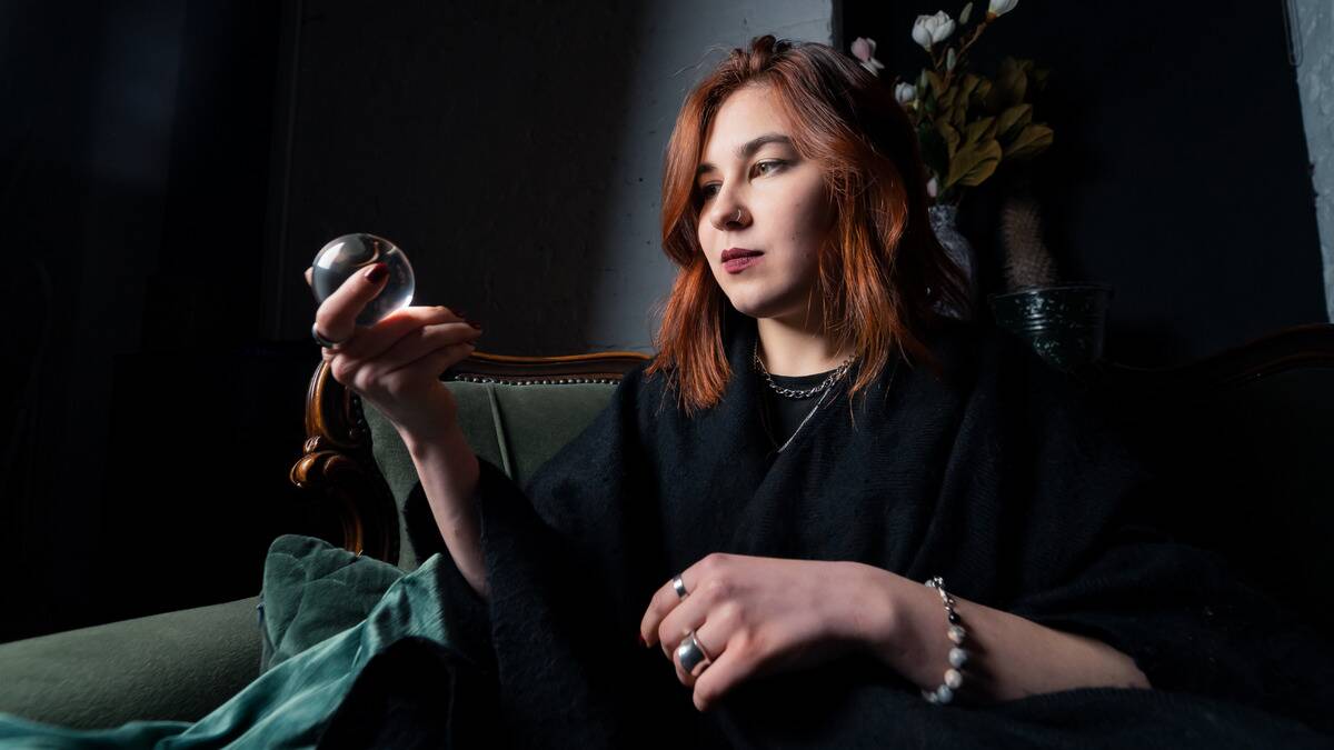 A woman sitting on a couch looking into a crystal ball that she's holding in one hand.