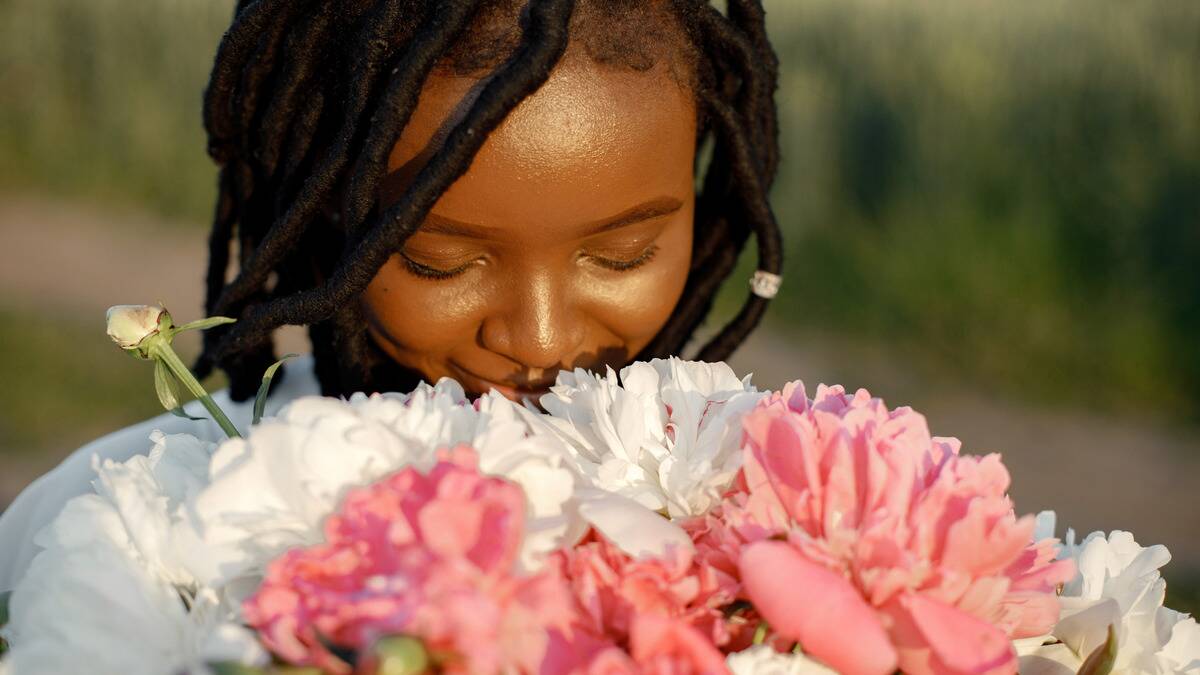 A close shot of a woman with her eyes closed tilting her head down to smell a bouquet of flowers.