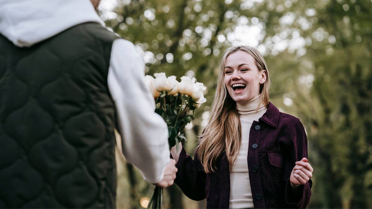 A man handing his girlfriend, who's smiling excitedly, a bouquet of white roses.