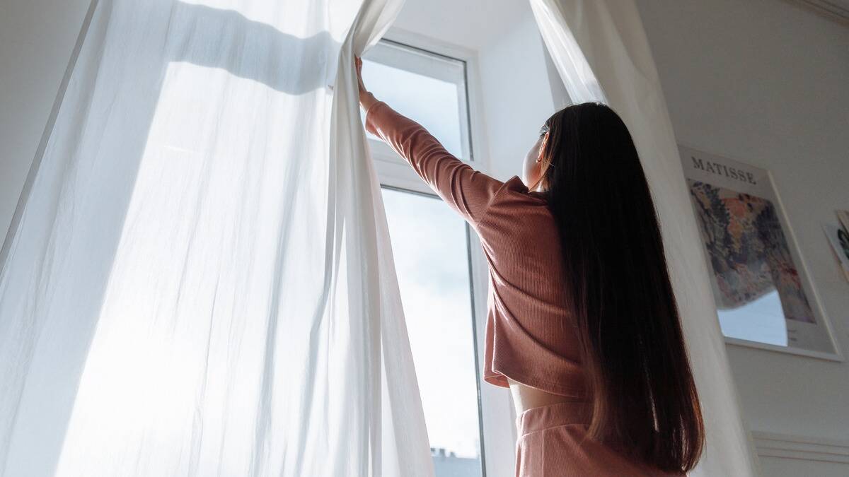 A low shot of a woman pushing open the curtains in front of her window.