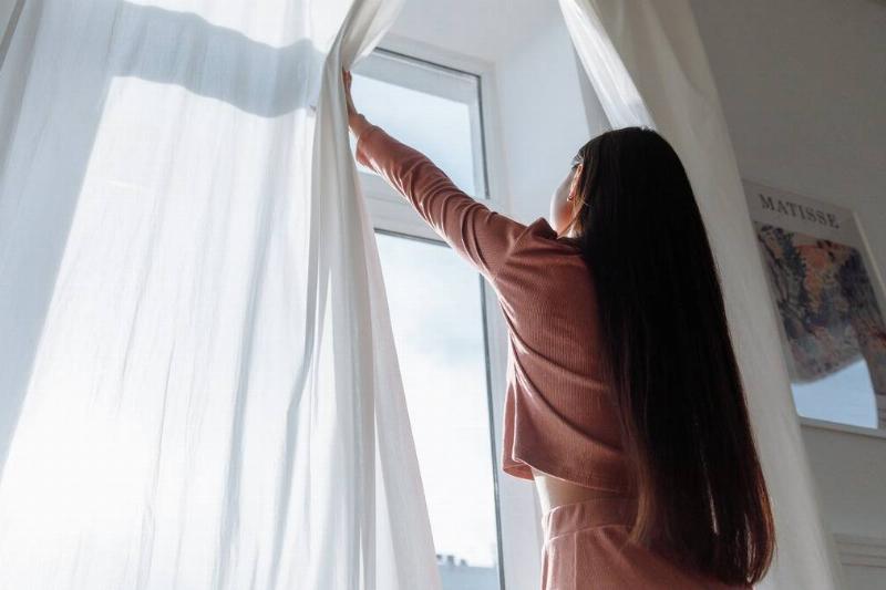 A low shot of a woman pushing open the curtains in front of her window.