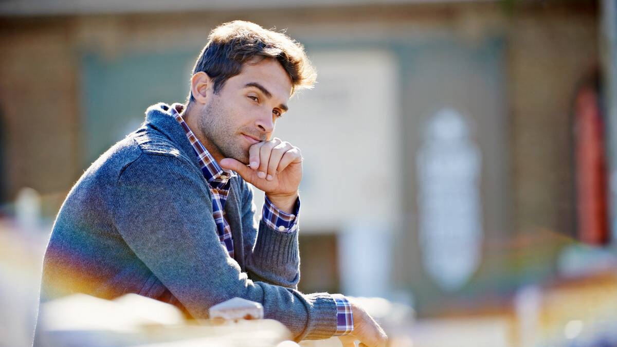 A man sitting outside, hand on his chin, looking thoughtful.