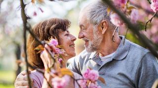 A couple standing with their faces very close together under a tree with pink flowering blossoms.