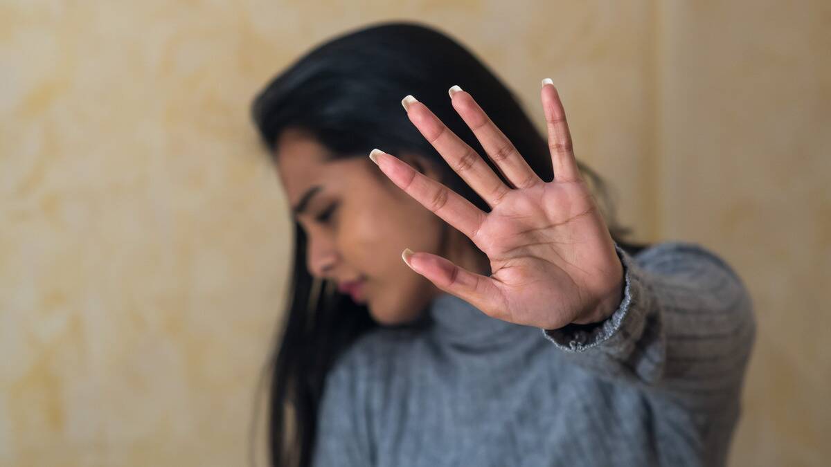 A woman holding a hand out in front of her face and looking away, saying no.