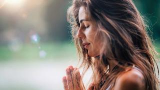 A close shot of a woman's face in profile, eyes closed, a peaceful smile, hands together in prayer.
