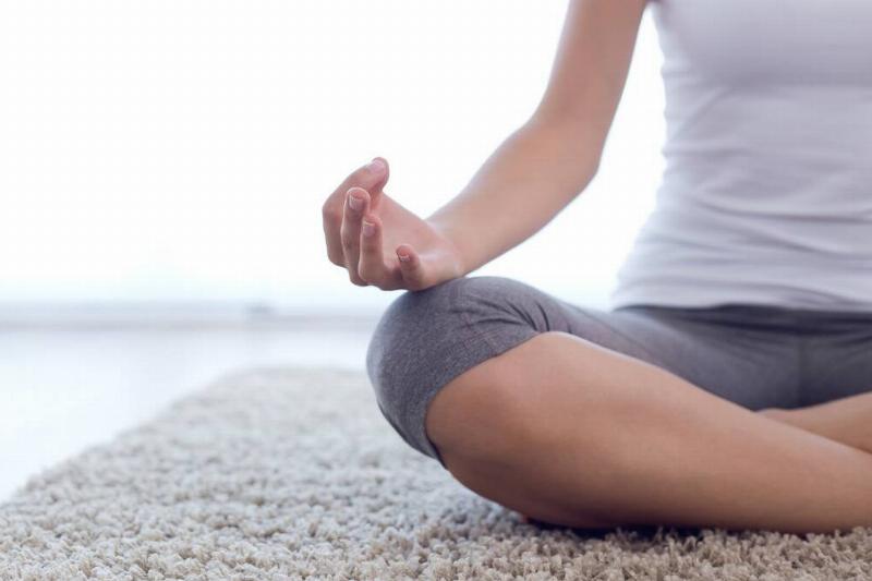 A close shot of a woman's hand and knee position as she meditates on a rug.