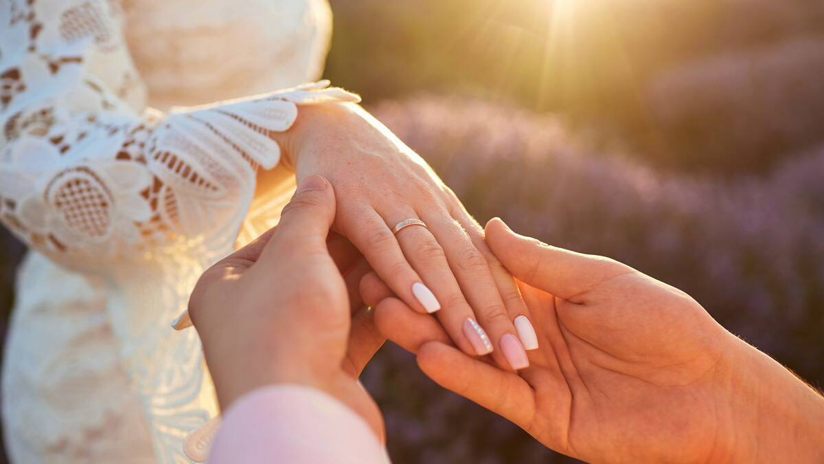 A close shot of a man holding his wife's hand with a newly placed wedding band on her ring finger on the day of their wedding.