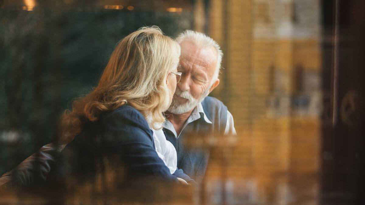 A couple seen through a window, sitting close and smiling peacefully.