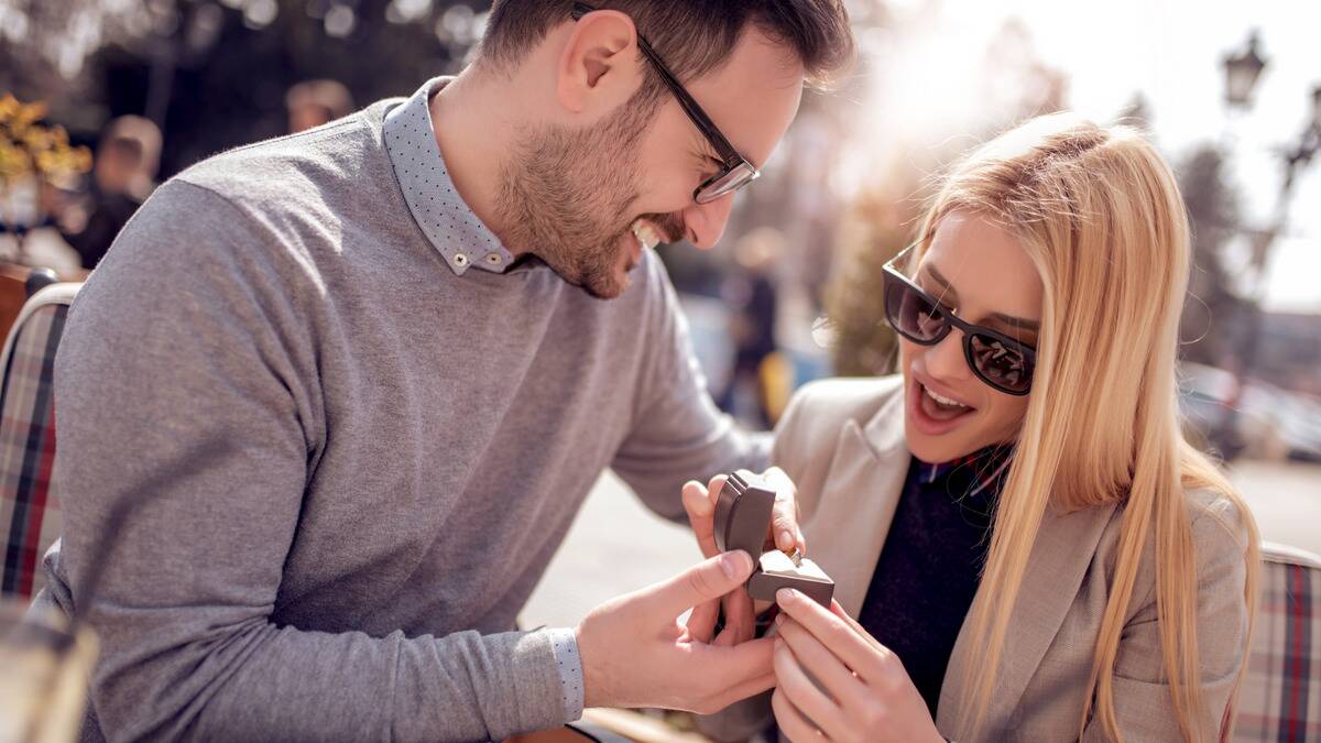 A close, angled shot of a man proposing to his girlfriend, who looks shocked and excited.