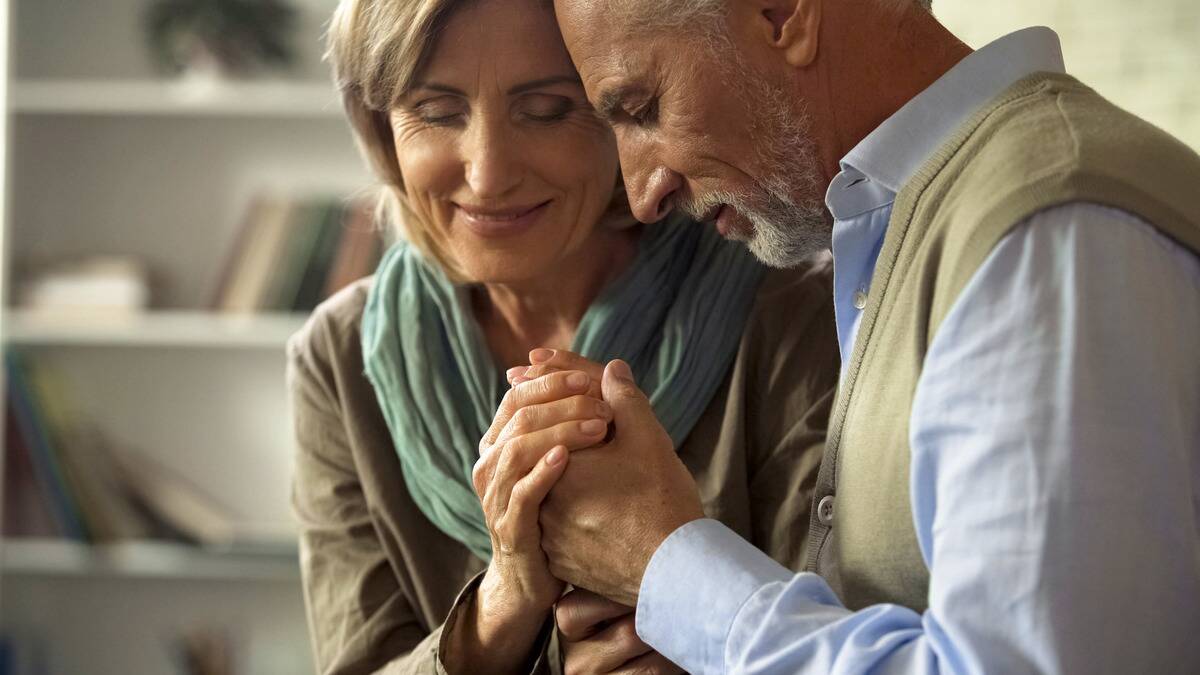 A close shot of a couple sitting together, eyes closed, heads together, hold each other's hands.