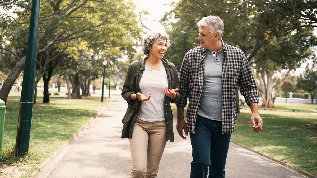 A couple walking through a park together, chatting as they do.