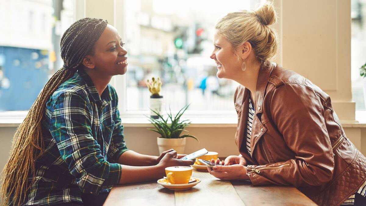 Two women sitting across from each other at a cafe, smiling as they chat.