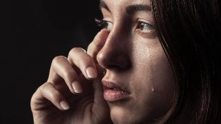 A close shot of a woman crying, hand up to wipe tears from one eye, the other crying freely.