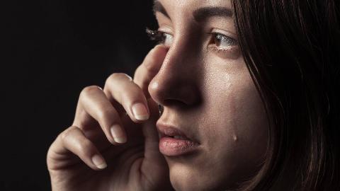 A close shot of a woman crying, hand up to wipe tears from one eye, the other crying freely.