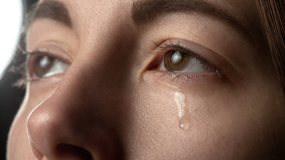 A closeup shot of someone's eye as they're crying, a single tear rolling down their cheek.