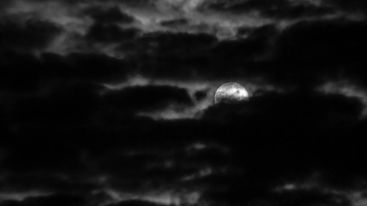 The full moon mostly covered by clouds in the night sky.