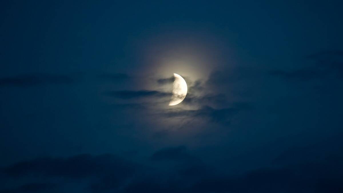 A half moon in a dark blue sky, half covered in clouds.
