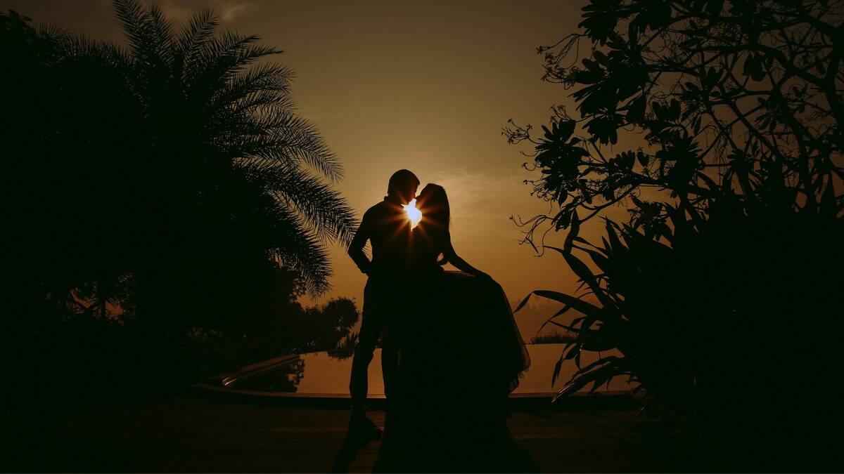 A silhouette of a couple dancing amid luscious plants and treats, the sun shining behind them.