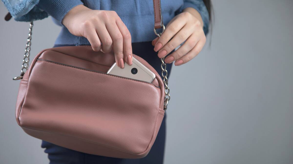 A close shot of a woman sneakily pulling her phone out of her purse.