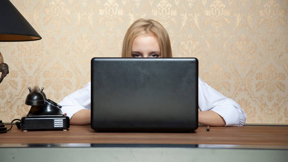 A woman sitting at a desk on her laptop, only her eyes and above able to be seen above the laptop's edge.