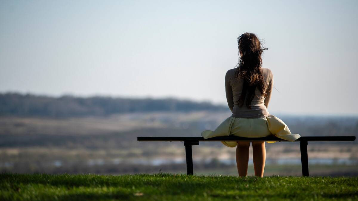 A woman sitting on a bench, looking out at the horizon.