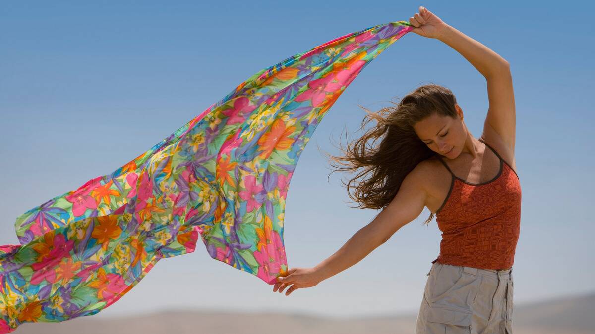 A woman standing outside, a colorful, floral shawl waving in the wind behind her.