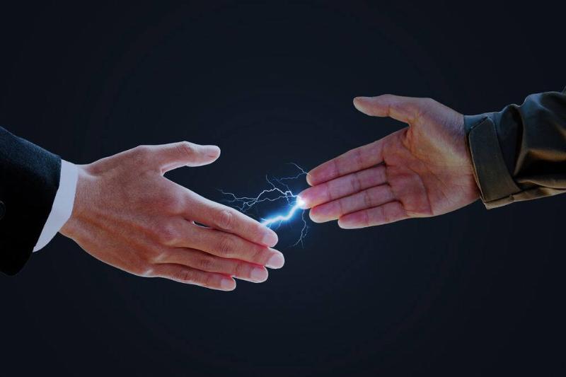 Two people reaching to shake hands, a static bolt edited between their fingers.