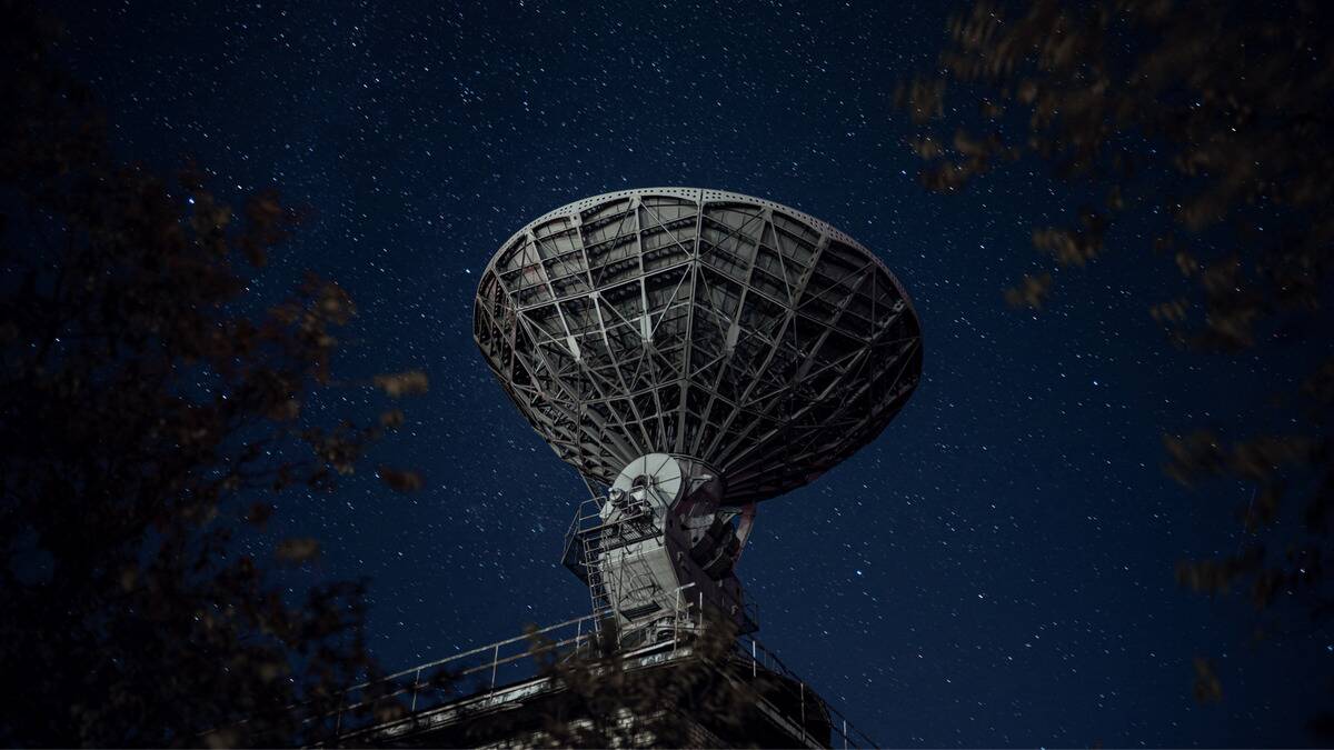 A large radio telescope pointed at the sky, stars seen above it.