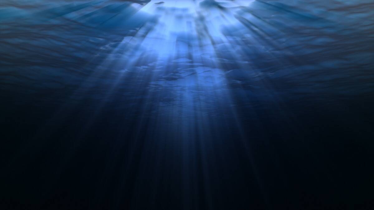 A photo from under water, beams of light shining through into the darkness.