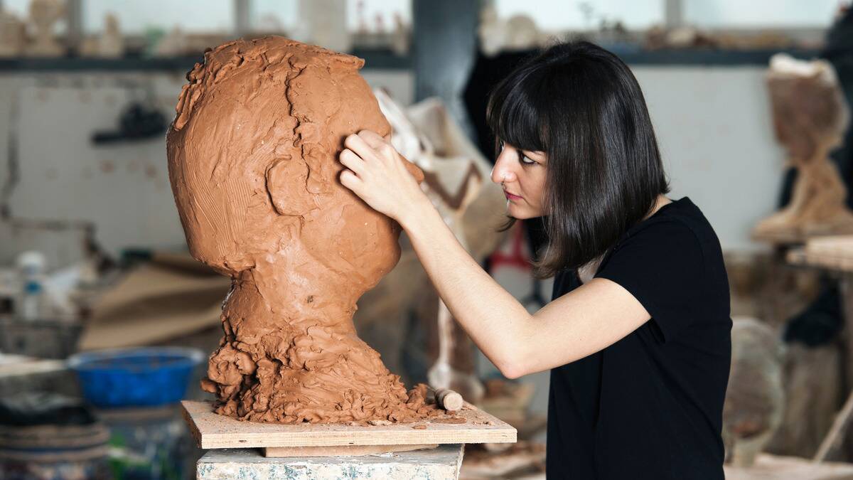 A woman working on a large sculpture of a male head.