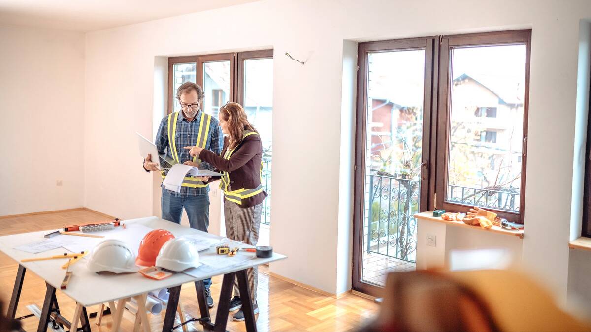 A couple discussing home renovations in front of a work table in an empty room, about to start working.