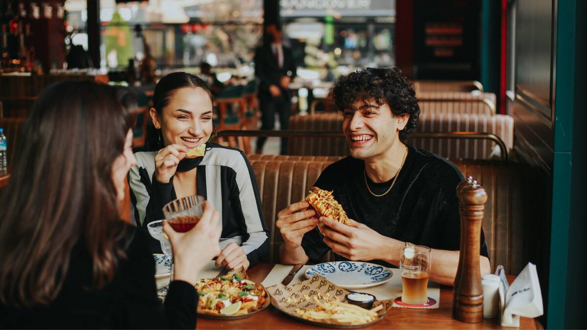 A group of friends sitting in a booth at a restaurant, smiling and chatting as they eat.