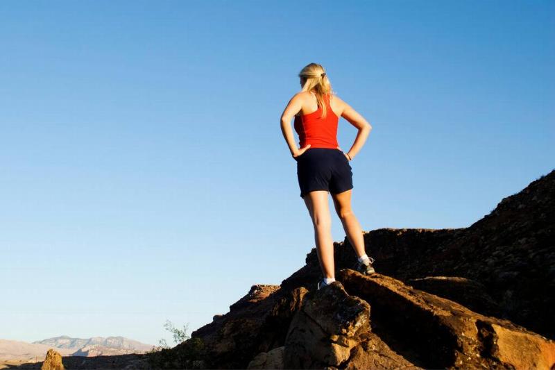 A woman standing on a rock, up on a summit, arms on her hips confidently.