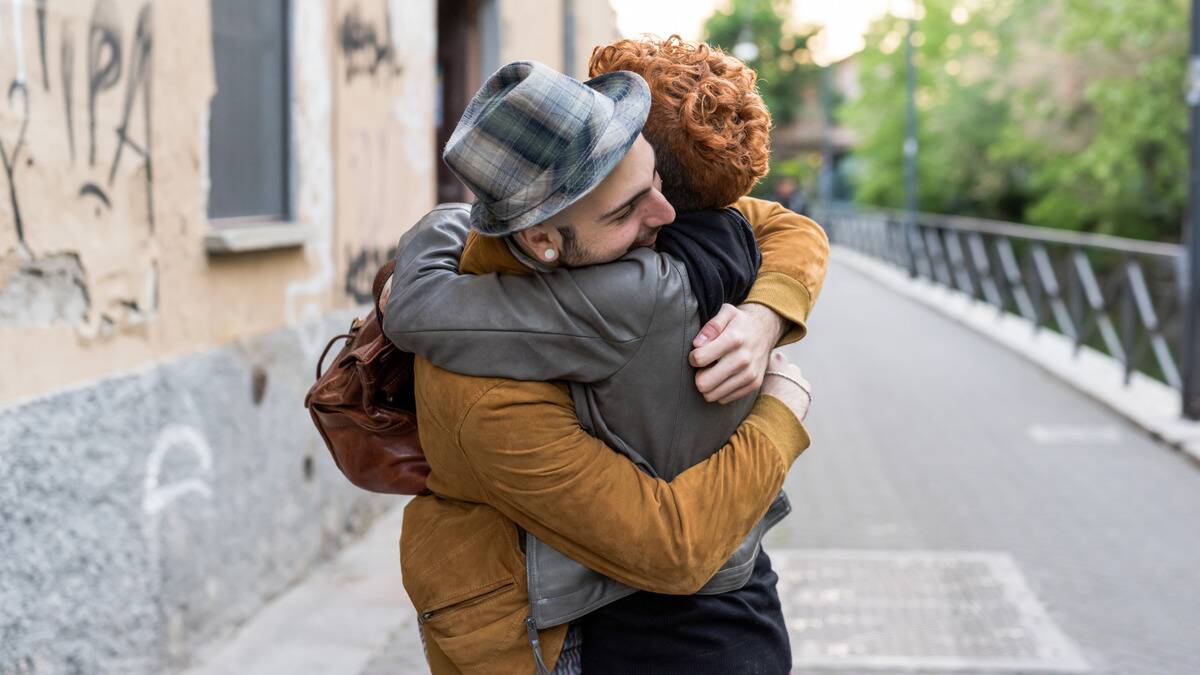 Two friends hugging tightly out on the street.