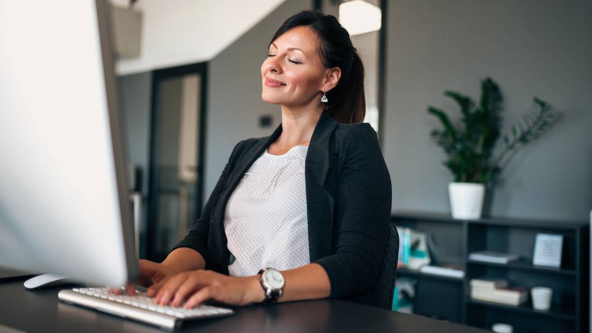 A woman at work, typing on her computer, her eyes closed contently.