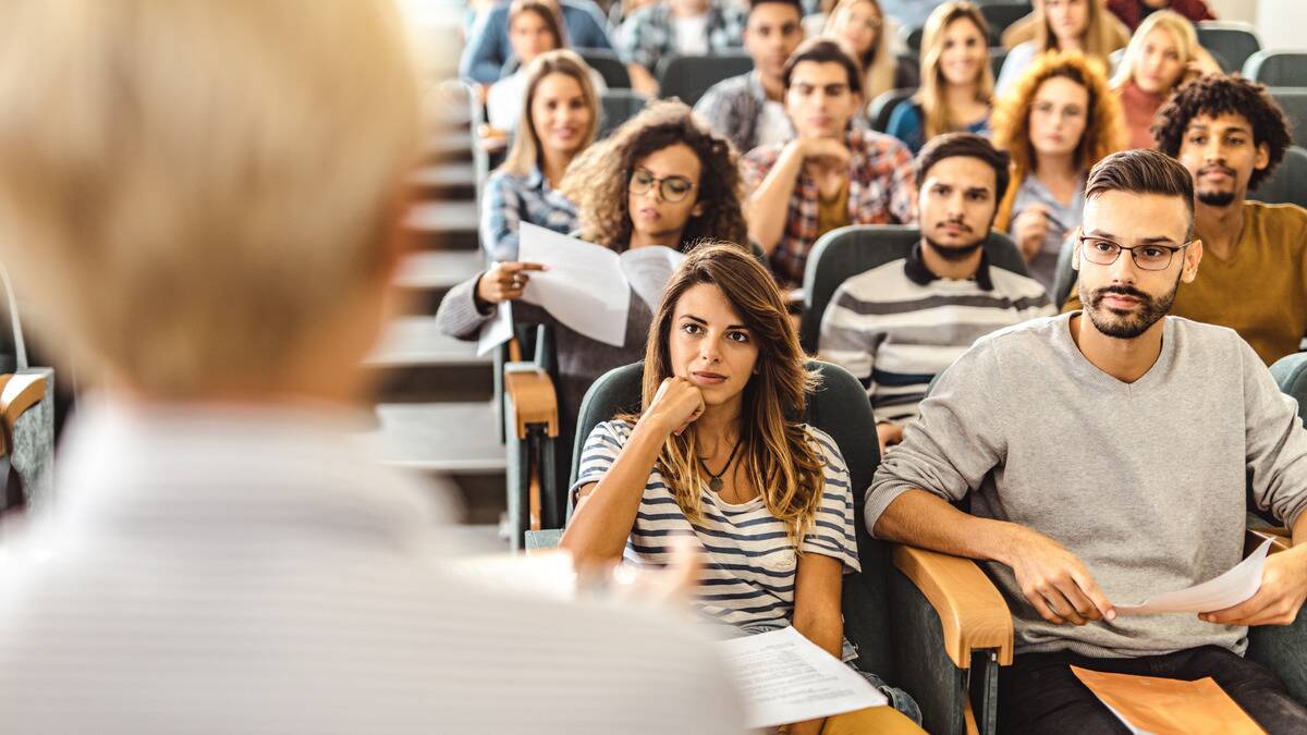 A university lecture hall class all looking at a teacher standing in the photos foreground.