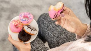 An over-the-shoulder shot of a woman holding a plate of small donuts, one in her hand, a bite taken out of it.