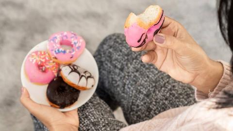 An over-the-shoulder shot of a woman holding a plate of small donuts, one in her hand, a bite taken out of it.