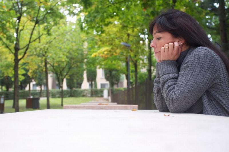 A woman sits at a park table by herself, chin in her hands.