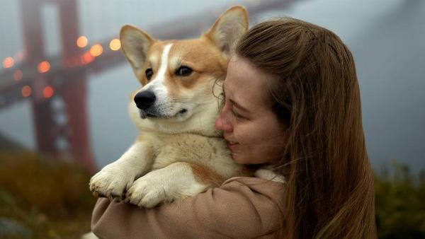 A woman holding a corgi close to her, smiling as she does.