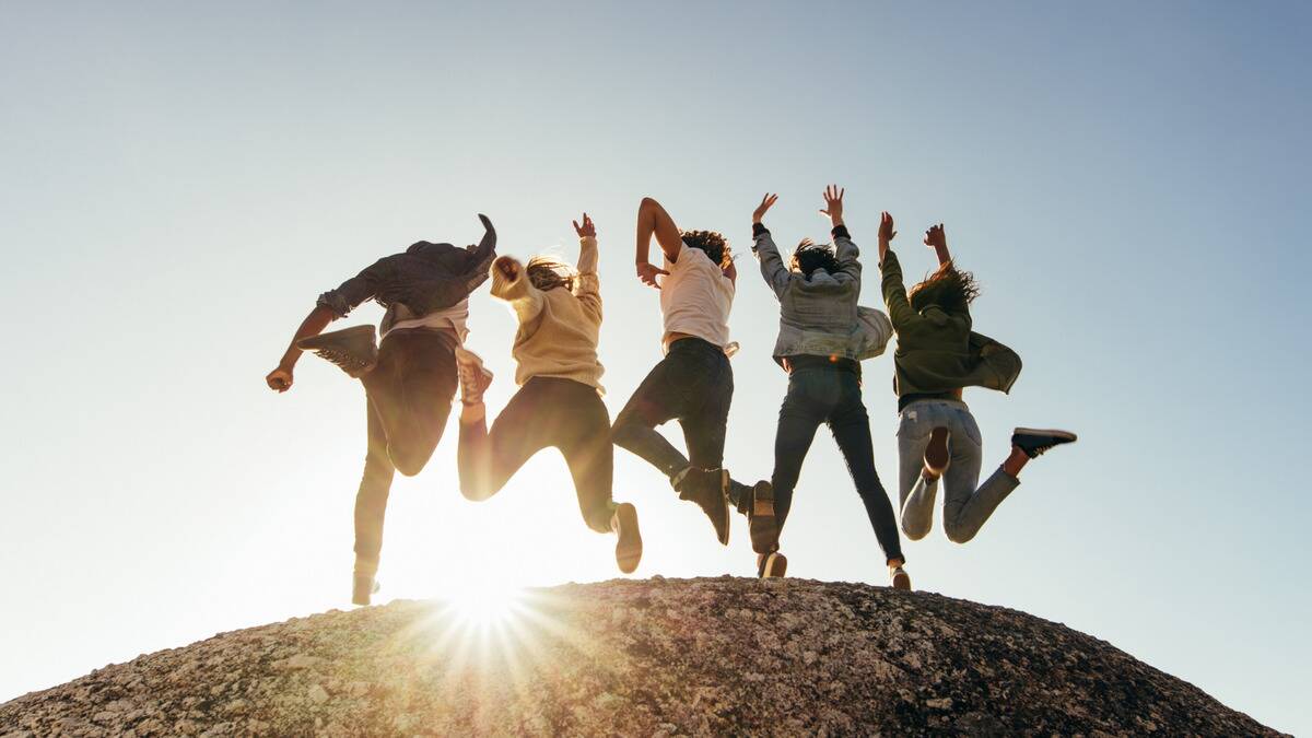 A group of friends on top of a hill jumping with their arms in the air.