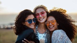 Three friends in colorful sunglasses posing close together, all hugging one another.