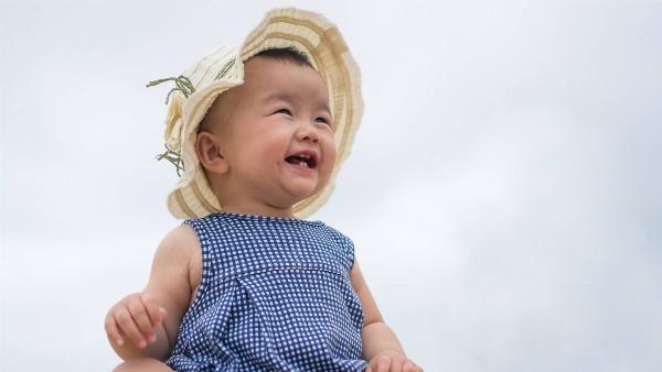 A baby in a sunhat smiling as she sits outside under a blue sky.