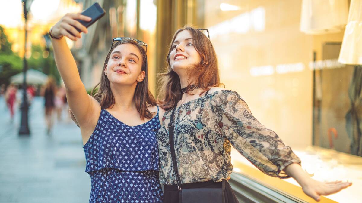 Two friends on the street taking a selfie, posing and smiling for it.