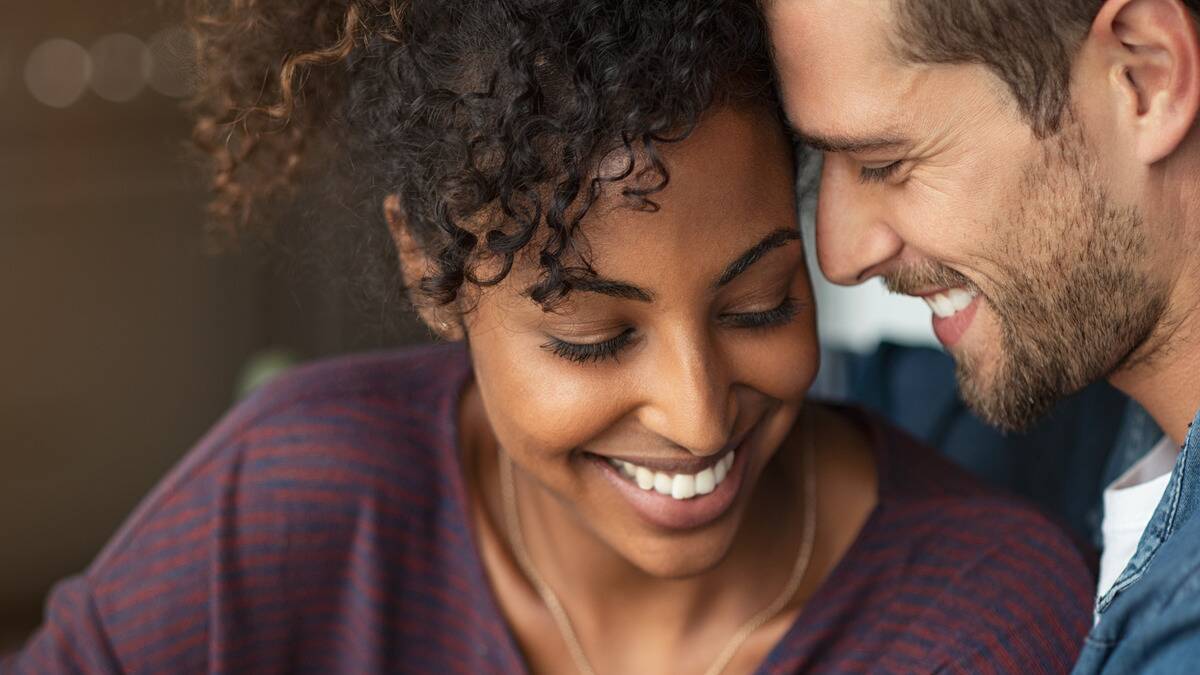 A close shot of a couple whose faces are close together, the man's forehead against her temple, both smiling peacefully.