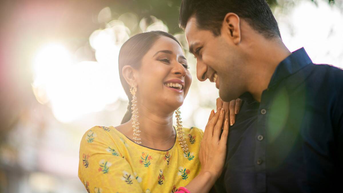 A low, close shot of a couple sitting next to one another laughing, the woman's hands on the man's shoulder.