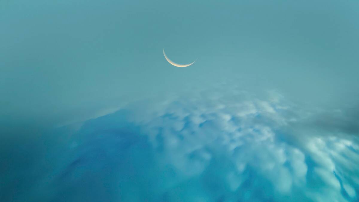 A sliver of a crescent moon visible in a blue sky above rolling clouds.